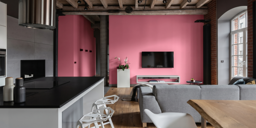 Nowoczesny salon z otwartą kuchnią w industrialnym loftowym stylu z r&oacute;żową ścianą i drewnianym sufitem.